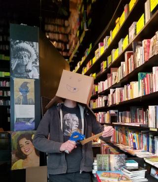 Buchhändler mit Karton auf dem Kopf. Auf dem Karton ist ein lächelndes Gesicht gezeichnet.