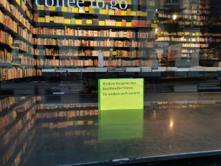 Ein Schild bei der Buchhandlung mit der Aufschrift: Winken Sie gerne den Buchhändler*innen. Sie winken auch zurück!