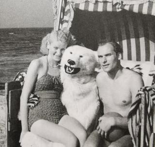Ein Paar in einem Strandkorb, zwischen ihnen jemand in einem Eisbärenkostüm.